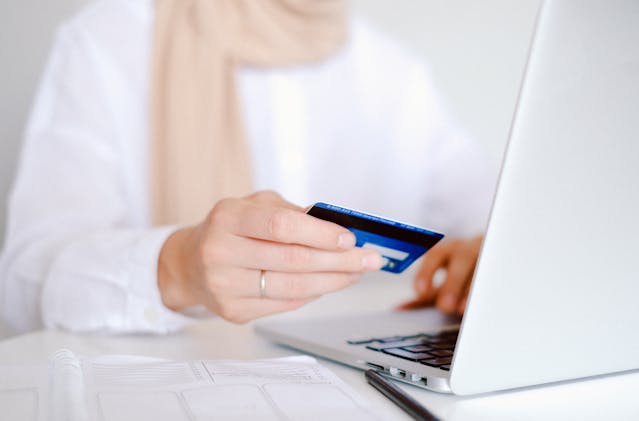 a hand holding a credit card infront of a laptop